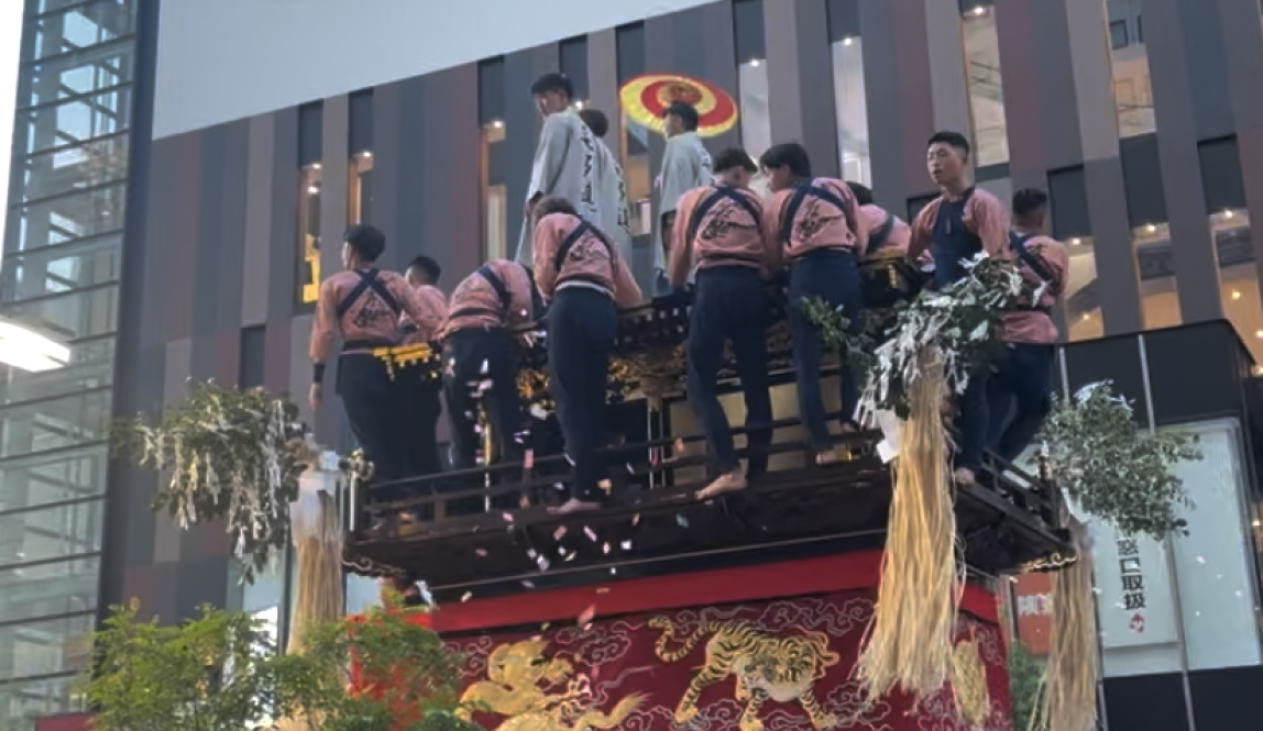 Dashi in a crowd with an Aeon mall in the background