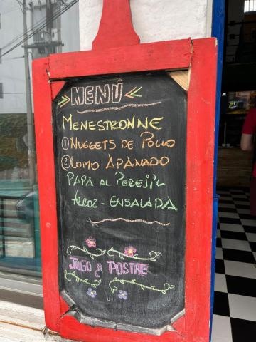 A chalkboard menu advertising minestrone soup, nuggets de pollo, lomo ampanado, rice, potatoes, salad, and juice and desert.