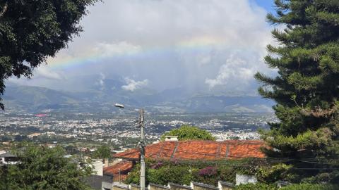 A valley containing lots of buildings clustered together, with a rainbow arcing above them.