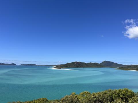 A large landscape of turquoise blue water is shown in the foreground. Tree cover and a clear sky are in the background.