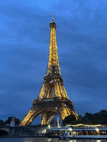 it is starting to get dark outside, the sky is dark blue; La Tour Eiffel is lit up and its reflection can be seen in the Seine river