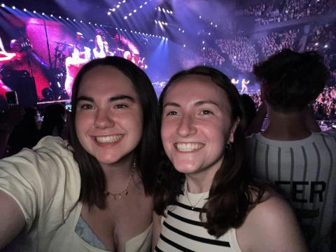 the photo is taken at concert; there are two smiling girls who took the selfie