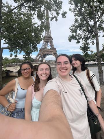 this is a 0.5 photo; in the photo there are 4 girls smiling; it is daytime in Paris and the Eiffel Tower is visible in the background