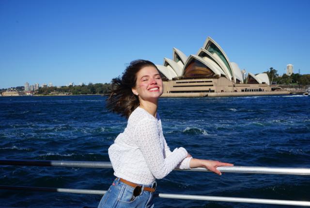 a student poses for a photo in front of Sydney Opera House from a boat in Sydney Harbour