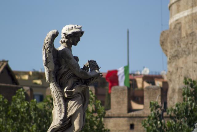 A close up shot of a statue of an angel near Castel Sant Angelo, with an Italian flag flying in the background.