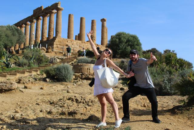 Two students stand in front of ancient Roman ruins, striking fun poses and smiling.