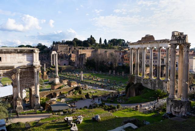 A view of the Roman forum, ancient Roman ruins and open green space.