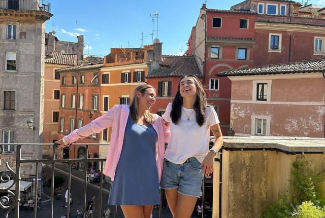Two students stand next to eachother laughing on a sunny rooftop in Rome.