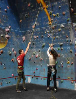 two dublin students standing in front of a rock climbing wall holding on to rope and smiling