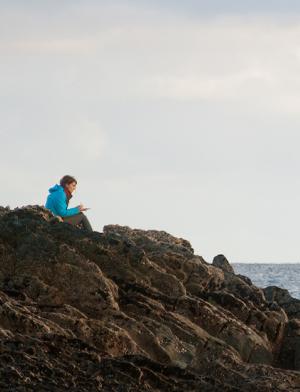 dublin student sitting on a rocky shore by the sea writing