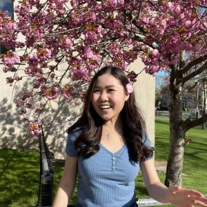 Headshot of Victoria Chen, standing in front of a pink flowering tree and smiling.