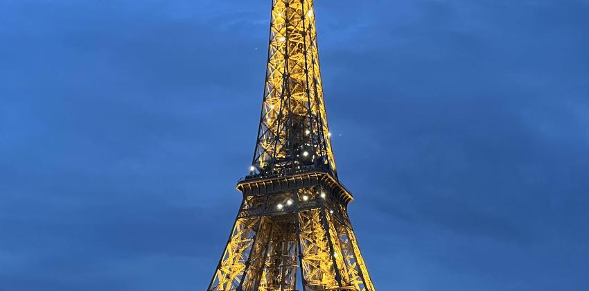 it is starting to get dark outside, the sky is dark blue; La Tour Eiffel is lit up and its reflection can be seen in the Seine river