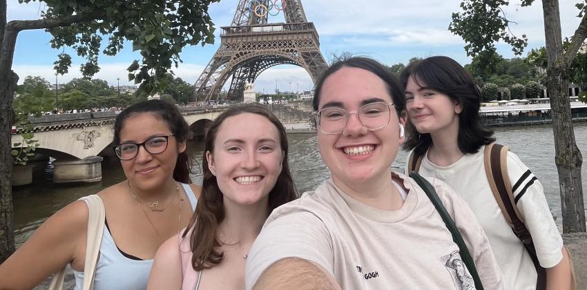 this is a 0.5 photo; in the photo there are 4 girls smiling; it is daytime in Paris and the Eiffel Tower is visible in the background