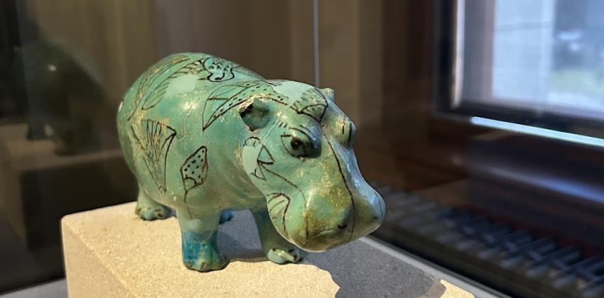 A teal Hippo statue set about the size of a squirrel atop a platform at Kunsthistorisches Museum in their Ancient Egypt collection